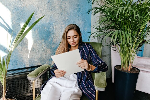 Mujer de negocios elegante posando en la oficina con periódico. Documentos de lectura de chica caucásica atractiva.