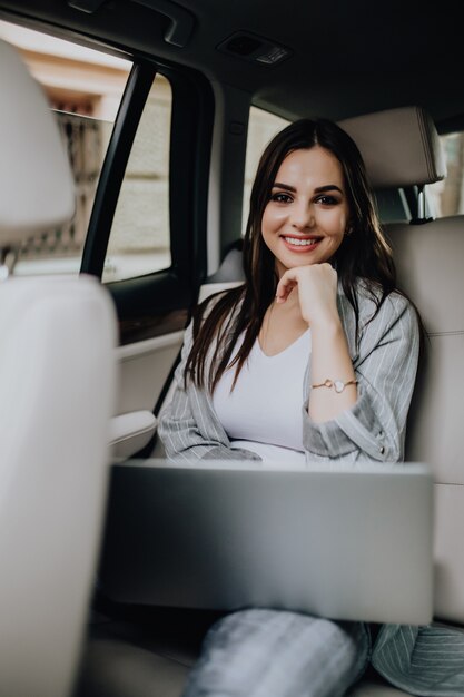 Mujer de negocios elegante sentado en el coche y trabajando en equipo portátil