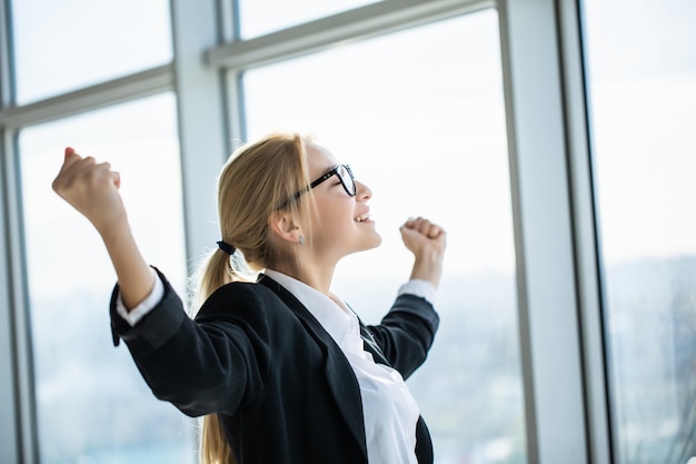 Mujer de negocios emocionada sostenga las manos levantadas los brazos celebrar la victoria en la oficina moderna