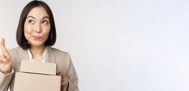 Mujer de negocios empresaria asiática esperanzada sosteniendo cajas con pedidos de clientes pidiendo deseos deseando y anticipando estar de pie sobre fondo blanco