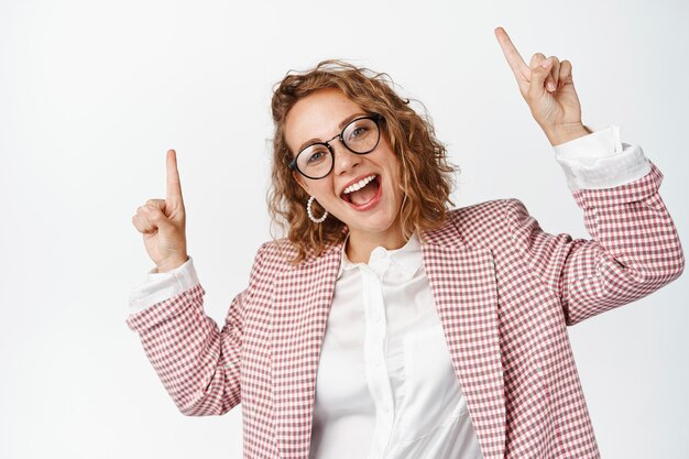 Mujer de negocios entusiasta apuntando con el dedo hacia arriba. Personas corporativas felices que muestran gráficos o diagramas en el espacio de la copia, de pie sobre fondo blanco.