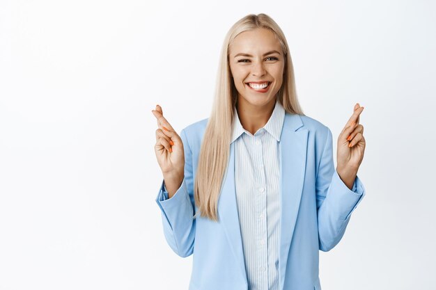 Mujer de negocios entusiasta cruza los dedos y pide deseos Vendedora rezando anticipando algo de pie sobre fondo blanco