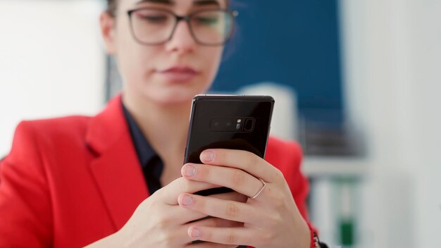 Mujer de negocios enviando mensajes de texto y navegando por Internet en un smartphone, trabajando en investigaciones financieras con informes estadísticos. Empleada que usa teléfono móvil en la oficina de inicio. De cerca.