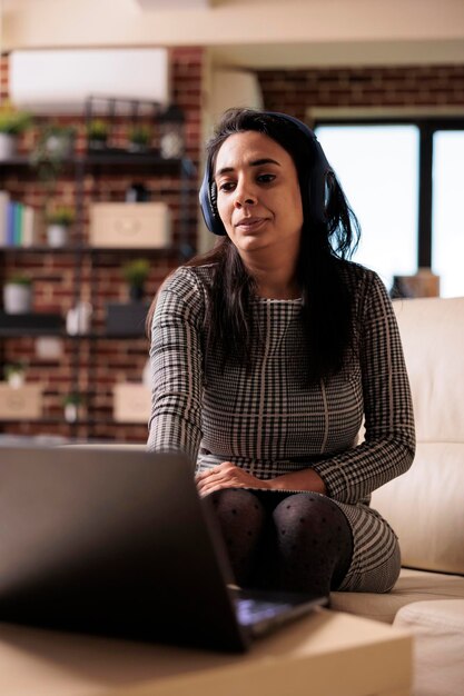 Mujer de negocios escuchando podcast o seminario web en auriculares con laptop, trabajando desde casa. Usar música en línea o asistir a una lección de clase en la red, navegar por el sitio web de Internet.