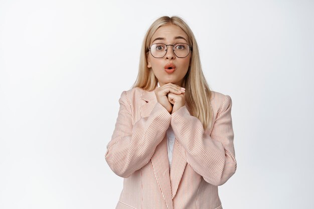 Una mujer de negocios esperanzada esperando con entusiasmo mirando fascinada esperando disfrutar de pie en traje y anteojos contra el fondo blanco