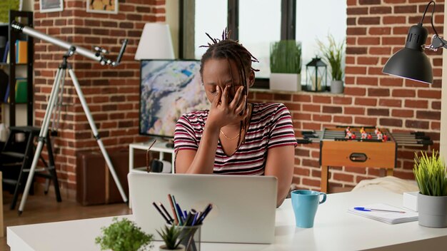 Mujer de negocios estresada con dolor de cabeza trabajando remotamente en una laptop en casa, sintiéndose cansada y frustrada por la fecha límite del trabajo. Haciendo trabajo remoto y sufriendo de migraña dolorosa, en tensión.