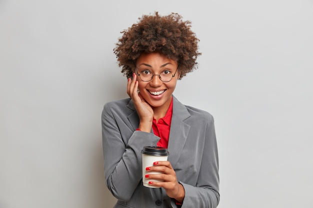 Una mujer de negocios exitosa y alegre de aspecto agradable toma un poco de café en la cafetería local, se relaja después del día de trabajo, sonríe positivamente con dientes blancos, bebe bebidas aromáticas