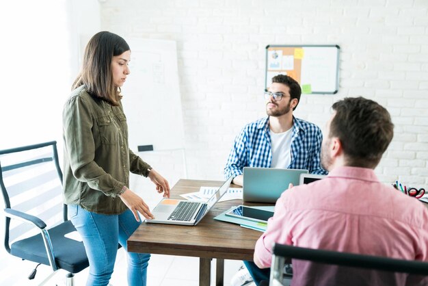 Mujer de negocios explicando el plan de negocios sobre la computadora portátil a colegas masculinos en una reunión en la oficina