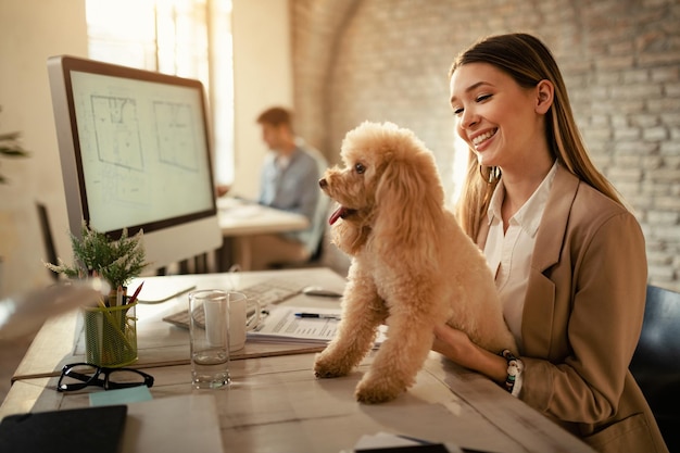 Mujer de negocios feliz disfrutando con su perro mientras trabaja en la oficina
