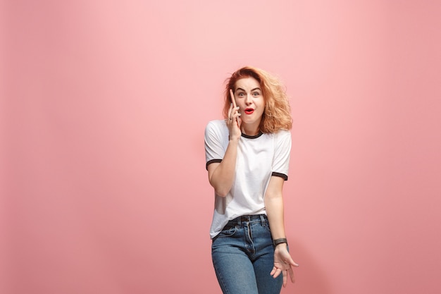 La mujer de negocios feliz está sonriendo y hablando en el teléfono inteligente contra el fondo de color rosa.