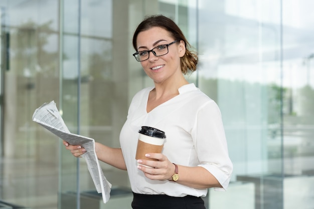 Mujer de negocios feliz leyendo el periódico y tomando café