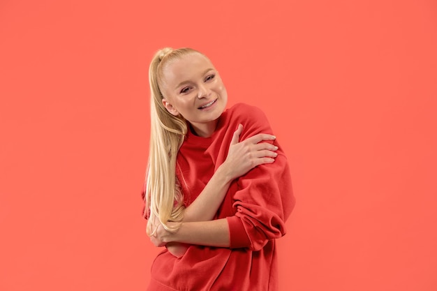 Mujer de negocios feliz de pie y sonriendo aislado sobre fondo de estudio de coral. Hermoso retrato femenino de medio cuerpo. Joven mujer emocional. Las emociones humanas, el concepto de expresión facial.