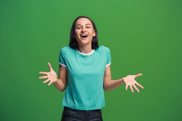 Mujer de negocios feliz de pie y sonriendo aislado sobre fondo verde de estudio. Hermoso retrato femenino de medio cuerpo. Joven mujer emocional. Las emociones humanas, el concepto de expresión facial. Vista frontal.