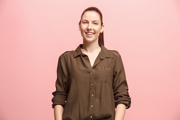 La mujer de negocios feliz de pie y sonriente contra la pared de color rosa.