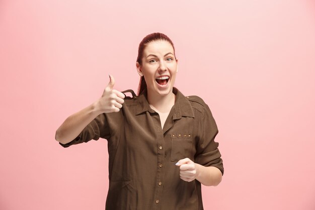 La mujer de negocios feliz de pie y sonriente contra la pared de color rosa.