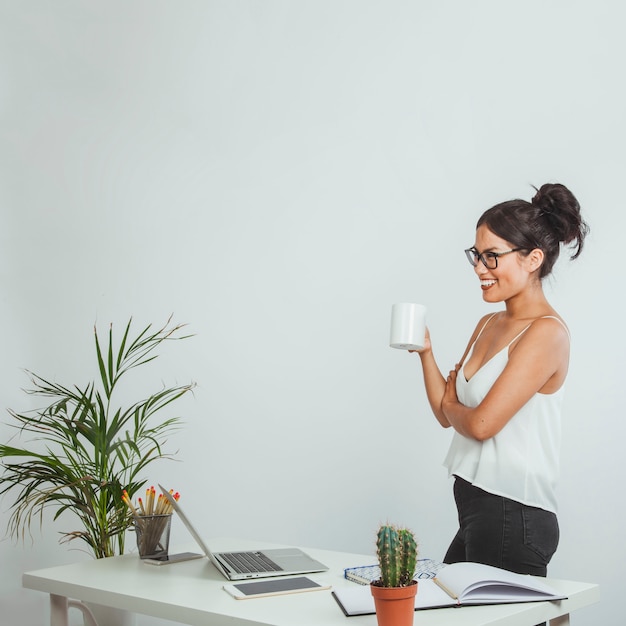 Mujer de negocios feliz posando con una taza de café en la oficina