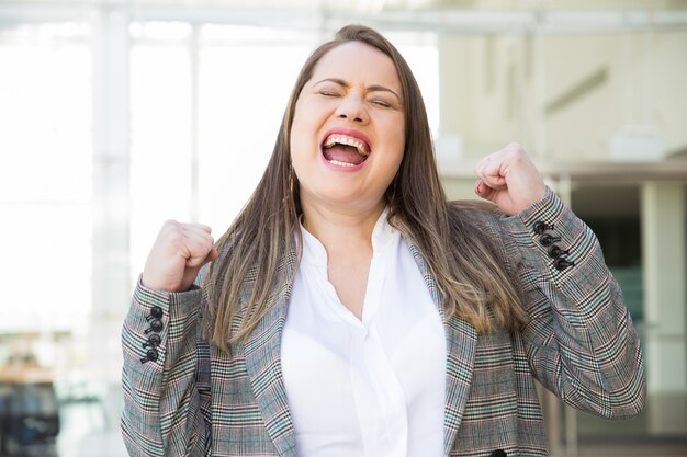 Mujer de negocios feliz que bombea los puños al aire libre