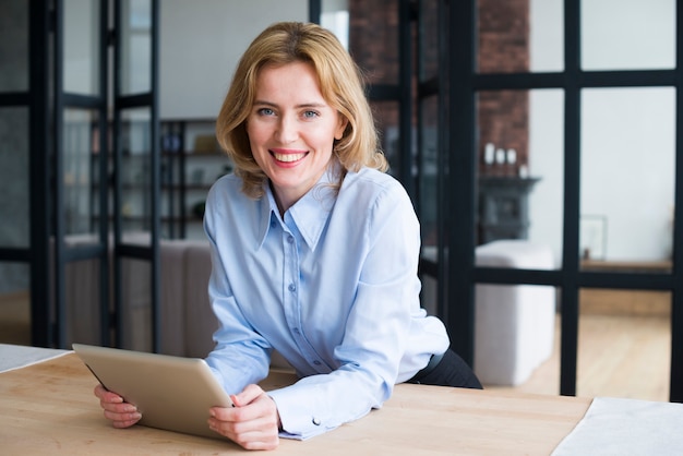 Mujer de negocios feliz que usa la tableta en la mesa