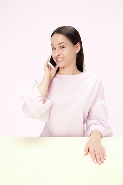 La mujer de negocios feliz sentada con teléfono móvil contra rosa.