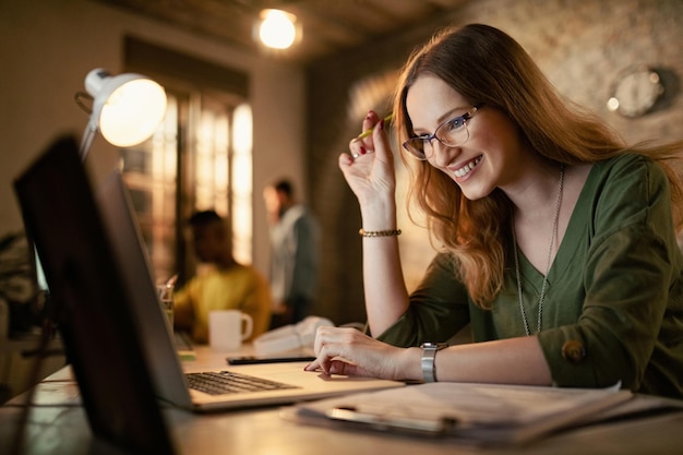 Mujer de negocios feliz trabajando hasta tarde en una computadora en la oficina