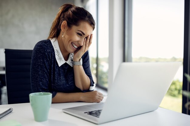 Mujer de negocios feliz usando computadora y citas en línea mientras trabaja en la oficina