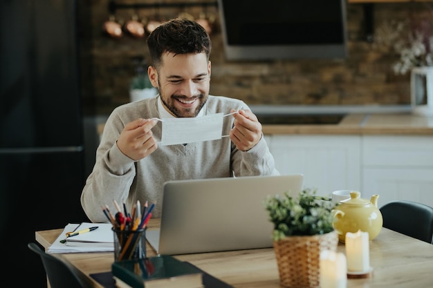 Mujer de negocios feliz usando mascarilla protectora mientras trabaja en una computadora en casa