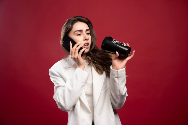 Mujer de negocios hablando por teléfono y mirando una taza de café