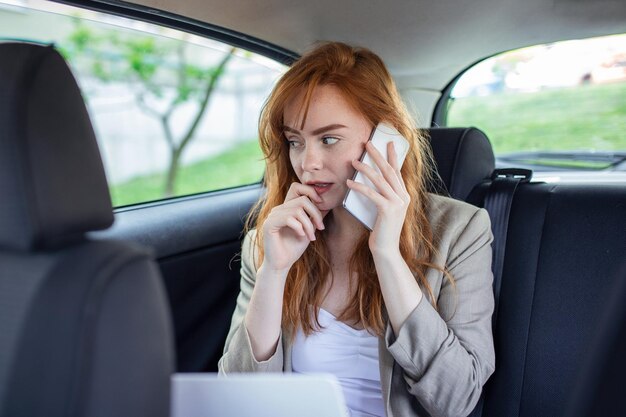 Mujer de negocios hablando por teléfono móvil y usando la computadora portátil en el auto