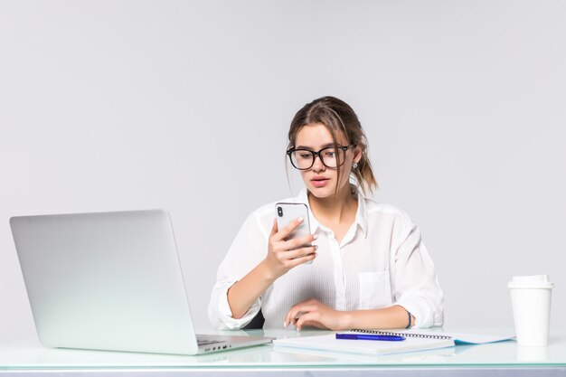 La mujer de negocios hermosa que sostiene el teléfono con la computadora en la oficina aislada en el fondo blanco