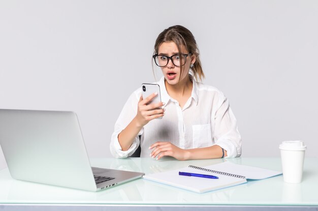 La mujer de negocios hermosa que sostiene el teléfono con la computadora en la oficina aislada en el fondo blanco