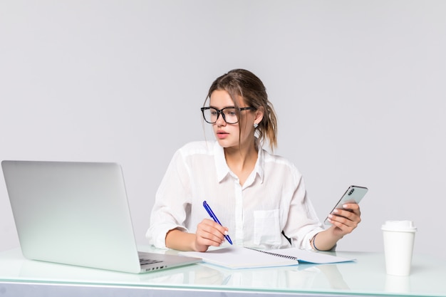 La mujer de negocios hermosa que sostiene el teléfono con la computadora en la oficina aislada en el fondo blanco