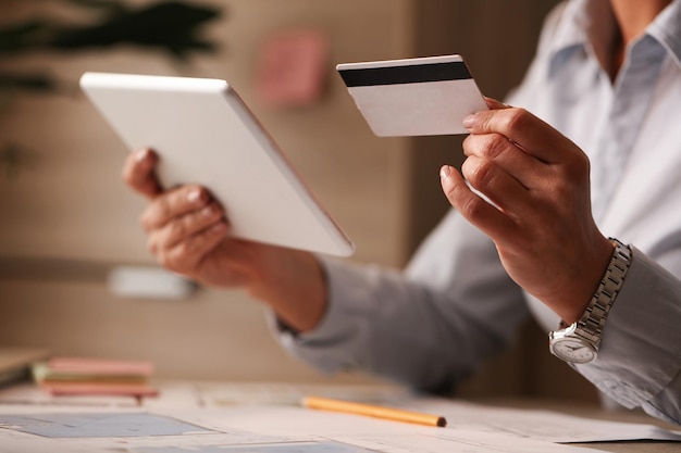 Mujer de negocios irreconocible que usa tarjeta de crédito y tableta digital mientras realiza operaciones bancarias en su oficina