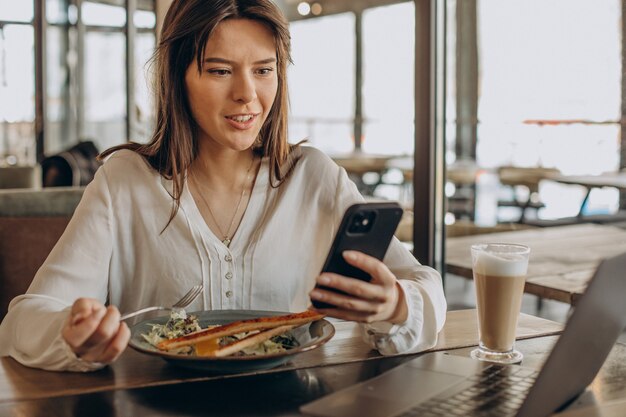 Mujer de negocios joven almorzando en un café y trabajando en equipo