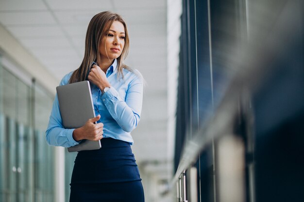 Mujer de negocios joven con la computadora portátil que se coloca en una oficina