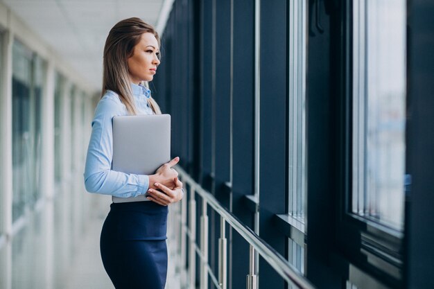 Mujer de negocios joven con la computadora portátil que se coloca en una oficina