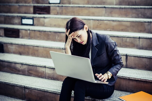 Mujer de negocios joven destacó desde la escalera de sesión de trabajo echar un vistazo en su portátil.