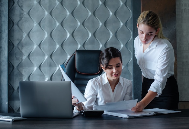 Mujer de negocios joven directora sentada en el escritorio de oficina con documentos de proceso de trabajo reunión de negocios trabajando con un colega para resolver tareas comerciales concepto colectivo de oficina