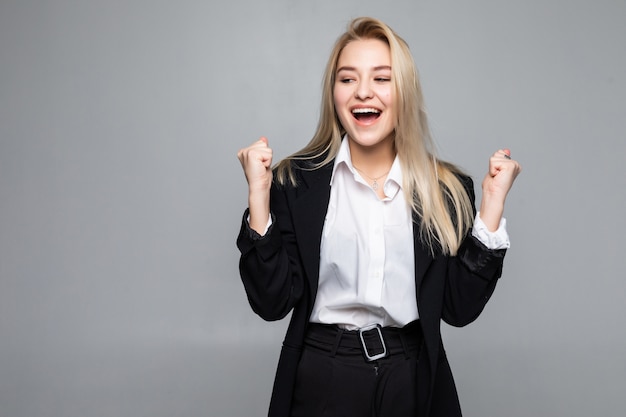 Mujer de negocios joven feliz haciendo gesto ganador, manteniendo los ojos cerrados posando aislado en la pared gris