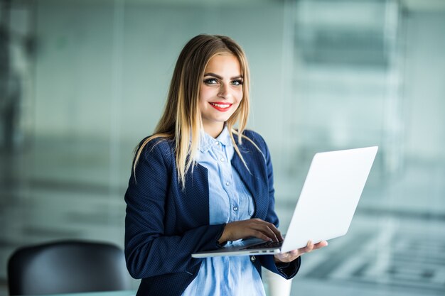 Mujer de negocios joven hermosa que usa la computadora portátil que se coloca cerca del escritorio en oficina