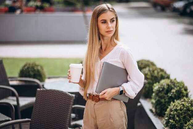 Mujer de negocios joven con laptop bebiendo café fuera de cafe