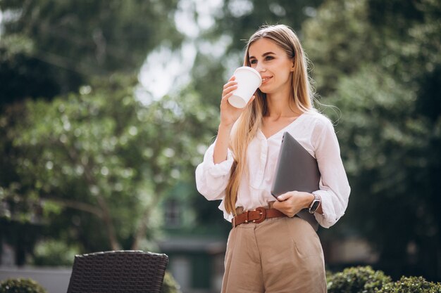 Mujer de negocios joven con laptop bebiendo café fuera de cafe