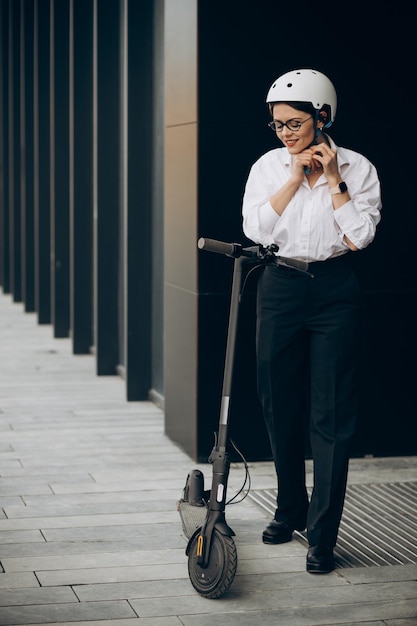 Foto gratuita mujer de negocios joven montando scooter eléctrico por centro de oficina