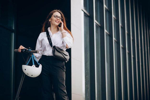 Mujer de negocios joven montando scooter y usando el teléfono