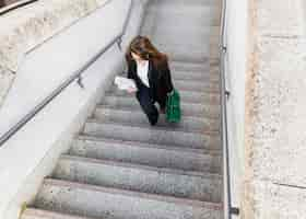 Foto gratuita mujer de negocios joven con el periódico y el bolso que suben las escaleras