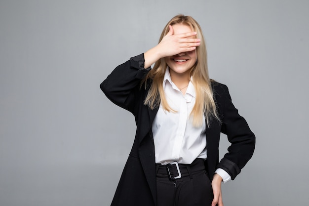 Mujer de negocios joven que cubre los ojos con las manos en la pared gris aislada