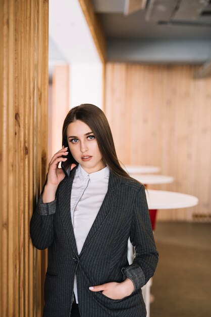 Mujer de negocios joven que habla por teléfono en la pared