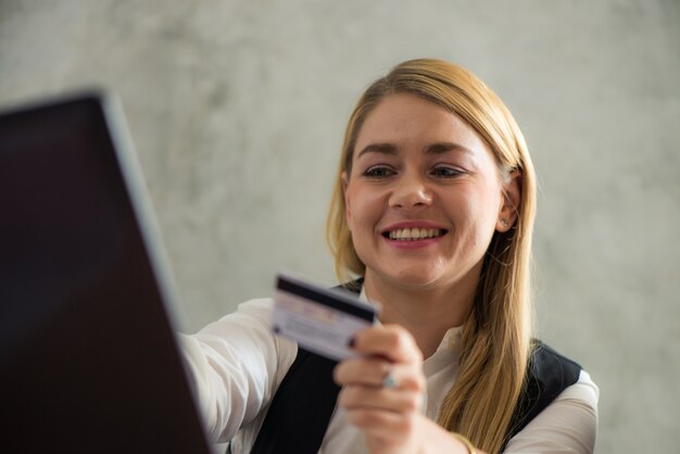 Mujer de negocios joven que sostiene la tarjeta de crédito y que usa la computadora portátil. Concepto de compras en línea. Vintage efecto estilo imágenes.