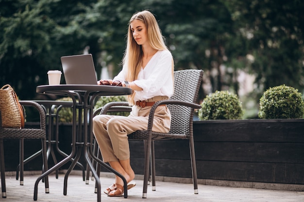 Mujer de negocios joven que trabaja en la computadora portátil afuera en un café