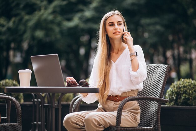 Mujer de negocios joven que trabaja en la computadora portátil afuera en un café
