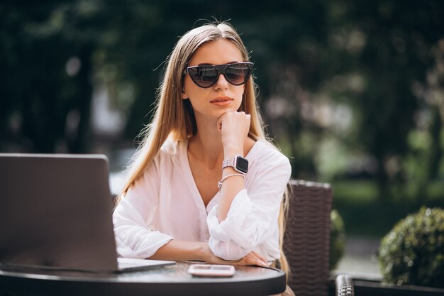 Mujer de negocios joven que trabaja en la computadora portátil afuera en un café